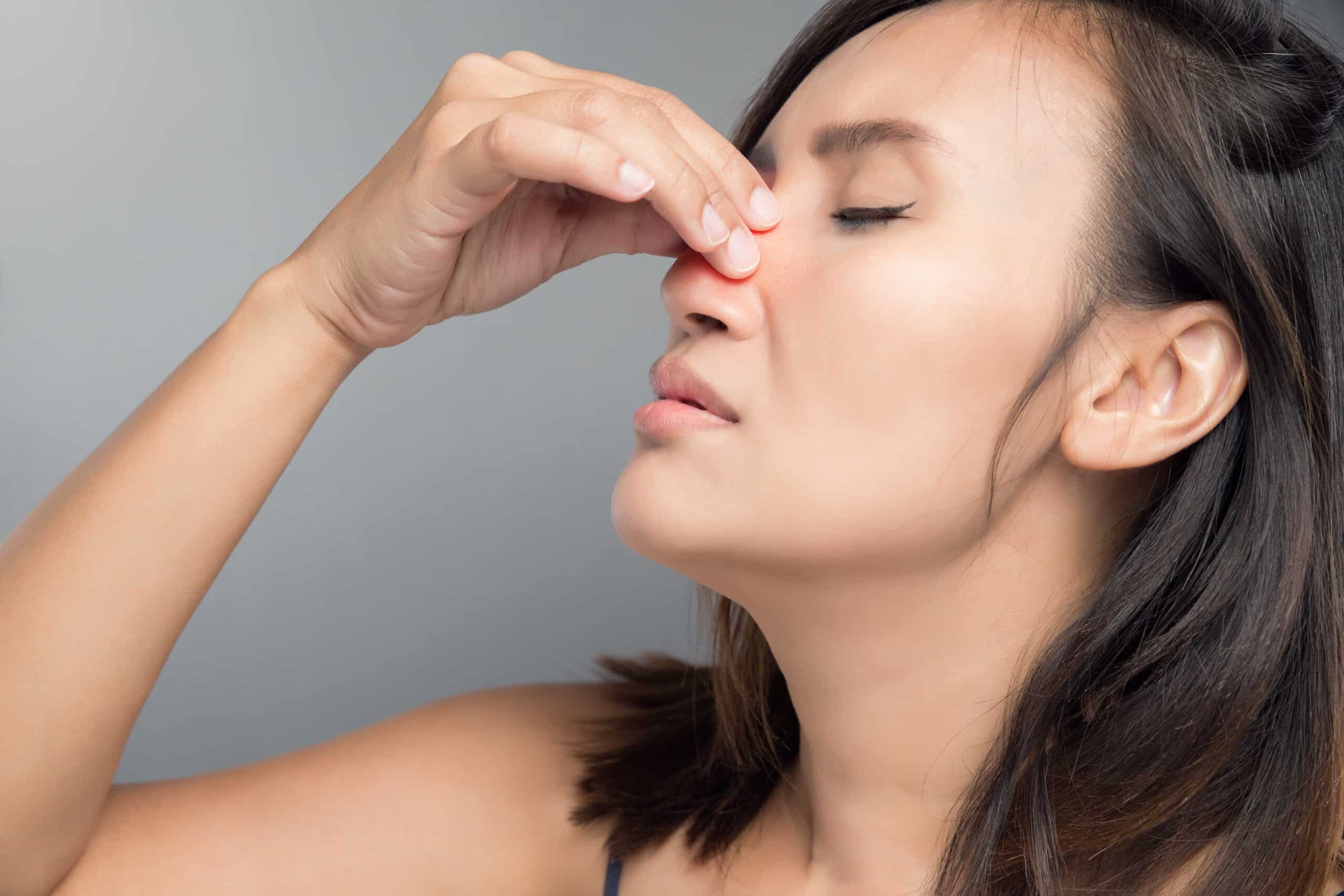 Woman holding the bridge of her nose in pain from a nasal polyp.