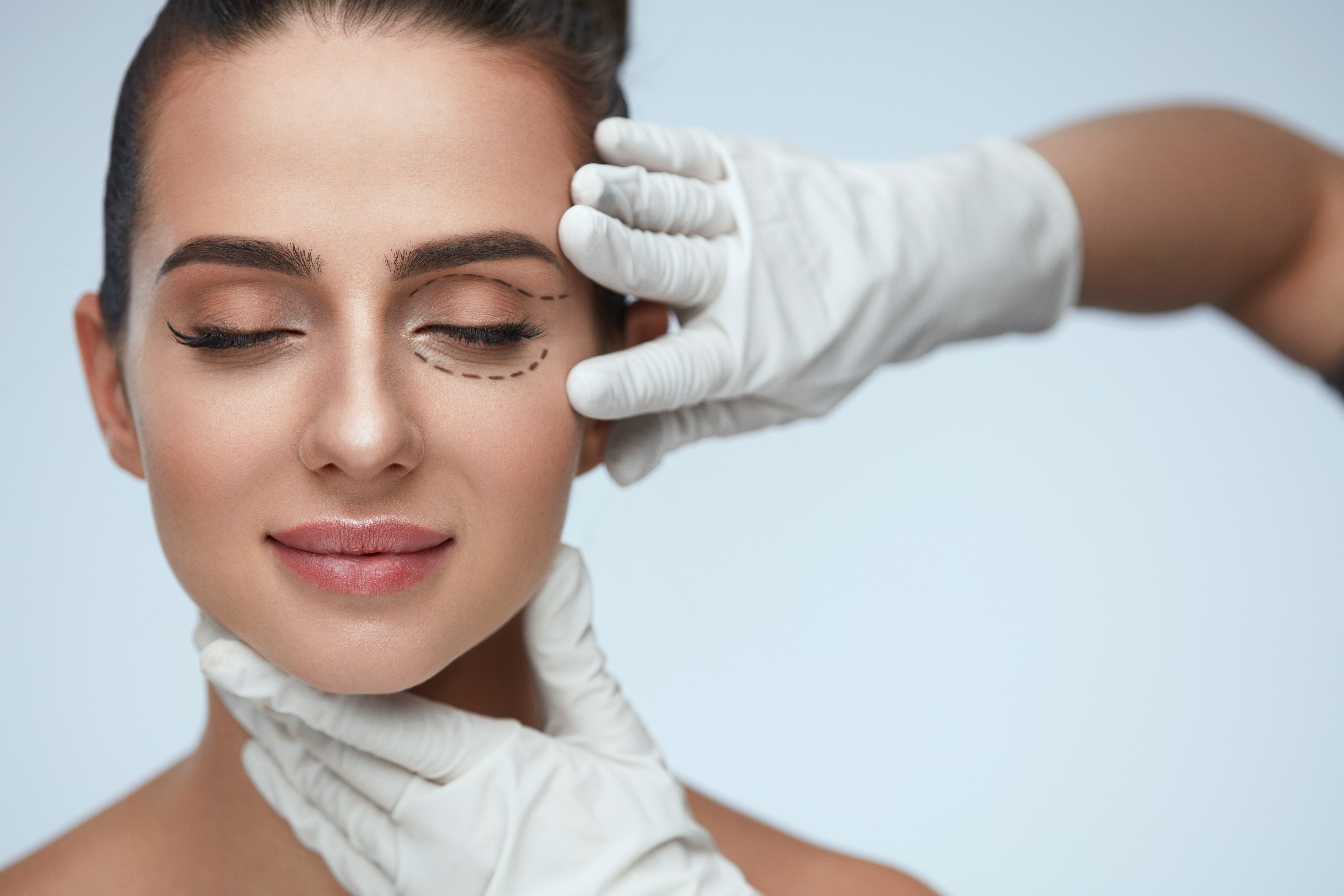 Head shot of woman preparing for eyelid lift procedure with the surgeon touching the woman's face and eyelid.